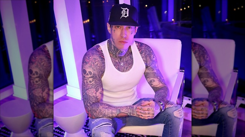 Trace Cyrus wearing a white tanktop while sitting in a white chair