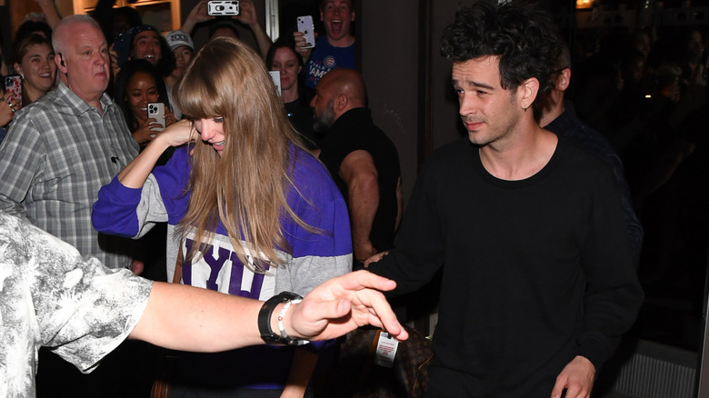 Taylor Swift and Matt Healy walking by a crowd