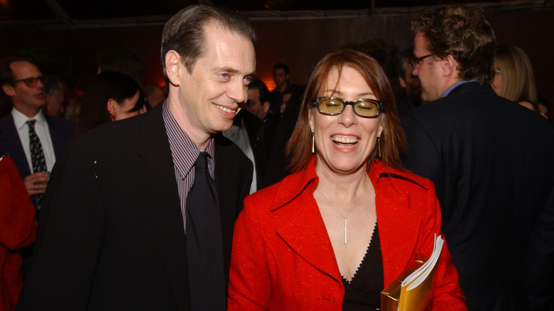 Jo Andres laughs in fashionable tinted sunglasses and a red overcoat at the Golden Globes next to her husband, Steve Buscemi