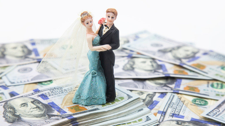 Wedding cake topper on top of hundred dollar bills. 