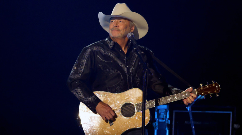 Alan Jackson looking wistful as he plays guitar on stage in a white cowboy hat
