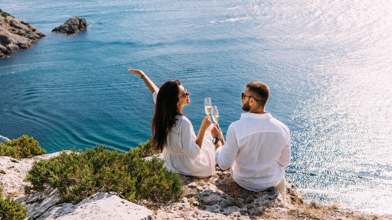 Couple drinks champagne on a beachside cliff