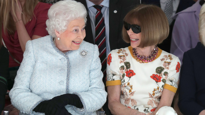 Anna Wintour wearing sunglasses while chatting with a beaming Queen Elizabeth II at London Fashion Week in 2018