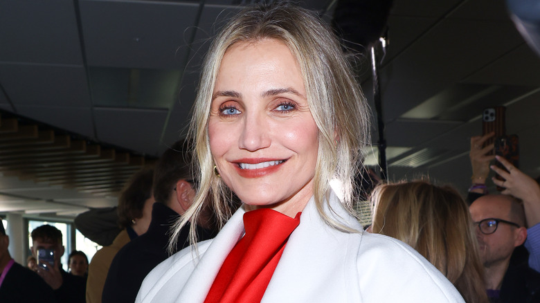 Cameron Diaz smiling while wearing red lipstick and a white coat