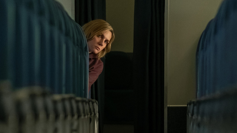 Rhea Seehorn sitting in amidst rows of empty seats in a scene from Pluribus