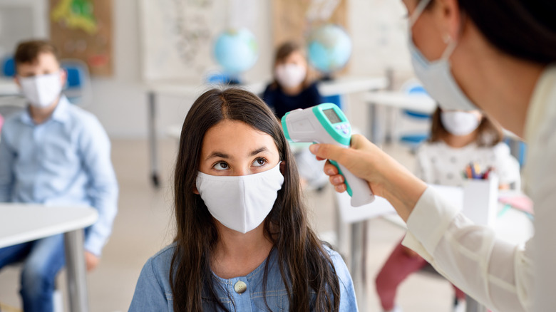 Teacher in mask checking student's temperature 