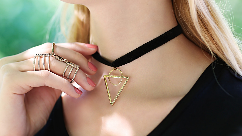 A woman lifting her hand to a pendant choker 