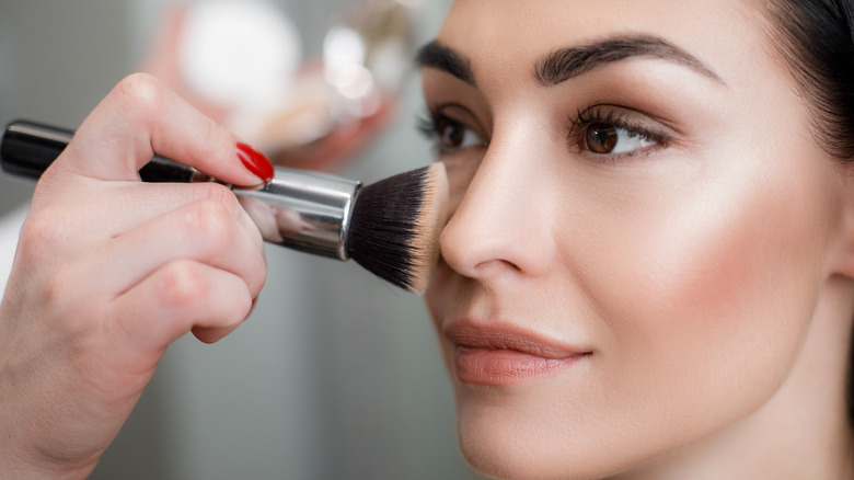 Makeup artist applying cream foundation to woman