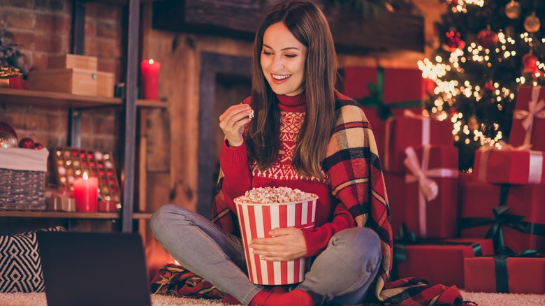 Smiling woman eats popcorn and watches laptop