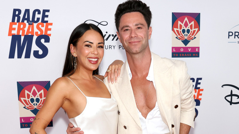 A smiling Janelle Parish posing with her arm resting on Sasha Farber's shoulder on the red carpet