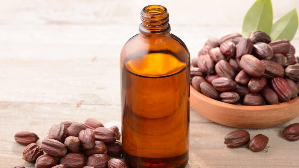 bottle of jojoba oil and seeds on wood board