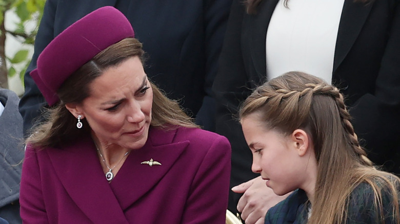 Kate Middleton wearing a violet blazer and hat while staring at Princess Charlotte while they celebrate VE day's 80th anniversay.