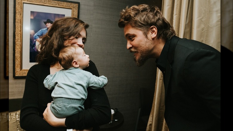 Bianca Rodrigues smiling and holding Rigel Grimes while Luke Grimes talks to his son