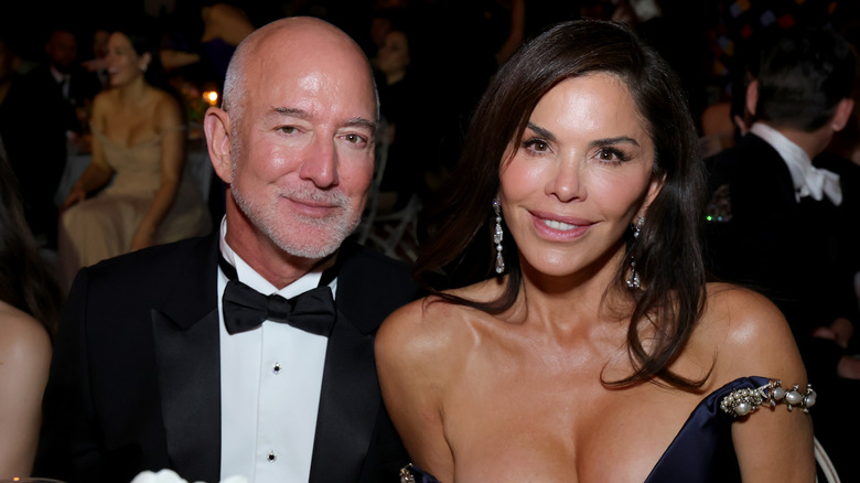 Jeff Bezos and Lauren Sanchez Bezos wearing formal wear and smiling while seated in a crowd.