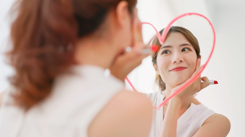 Girl gazing at lipstick heart on mirror