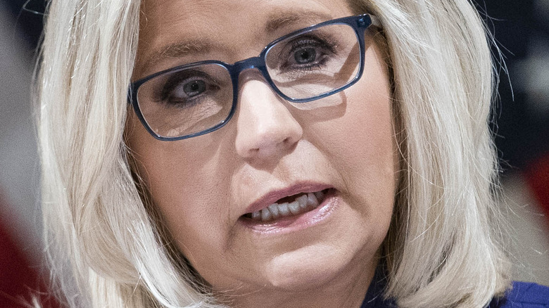 Liz Cheney wearing blue glasses in front of American flag