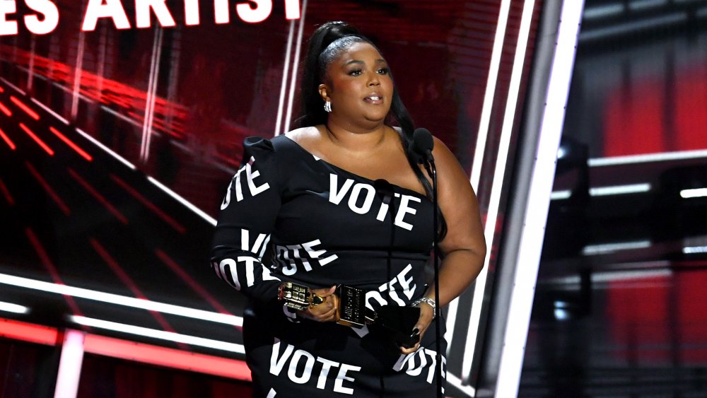 Lizzo accepting her award in a black dress with vote written on it in white