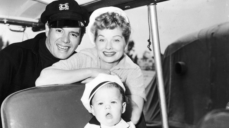 Black-and-white photo of Desi Arnaz and Lucille Ball posing on a boat with their baby daughter Lucie sitting in front of them