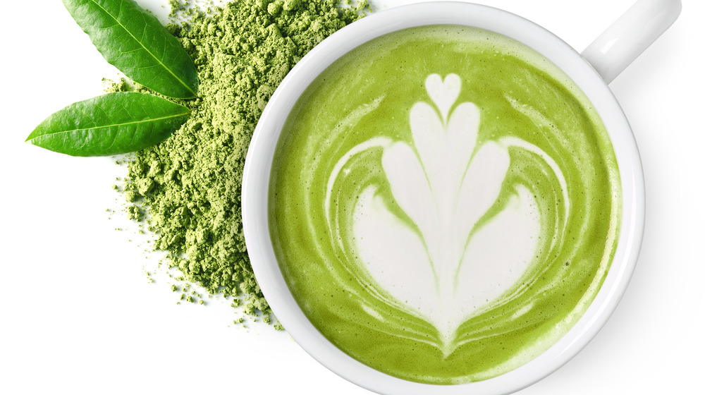 Matcha tea in a white mug with powder beside it.