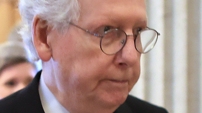 Mitch McConnell in a black suit, frowning