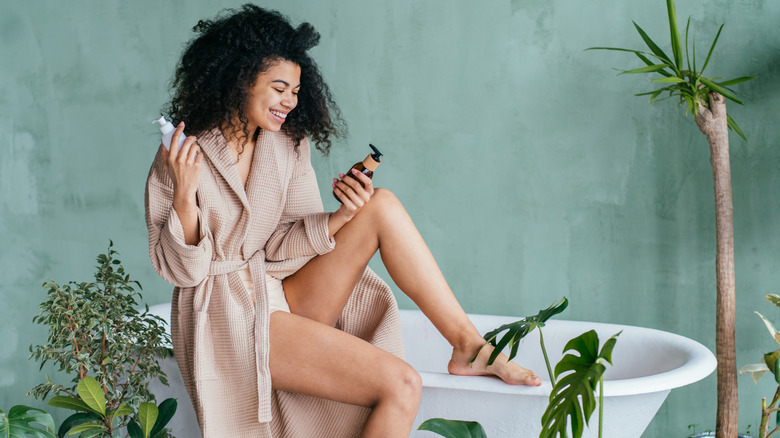 Woman sitting on a bathtub holding beauty products