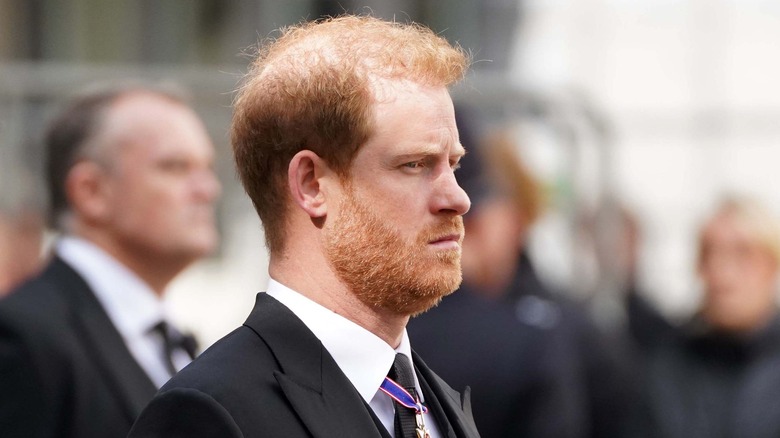Prince Harry stands with solemn expression