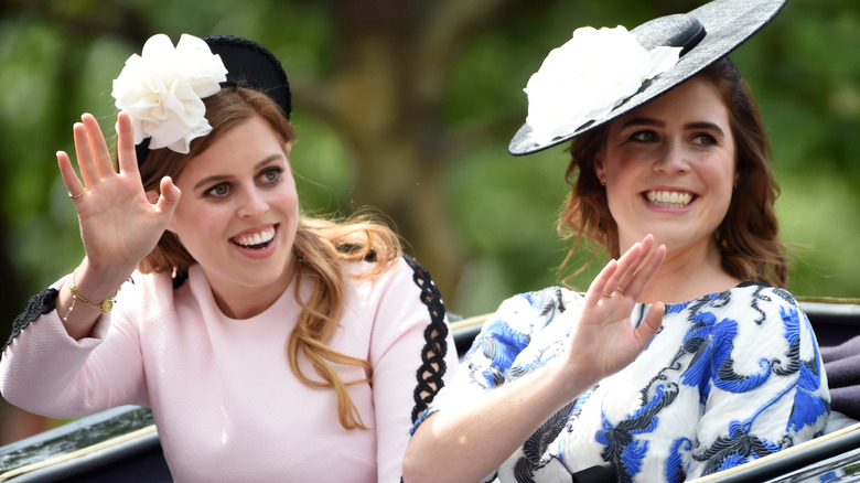 Princess Beatrice and Eugenie waving off camera as they sit in a carriage side by side