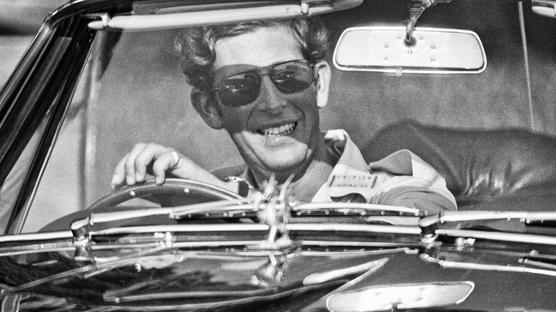 Black-and-white photo of a young King Charles III driving a car