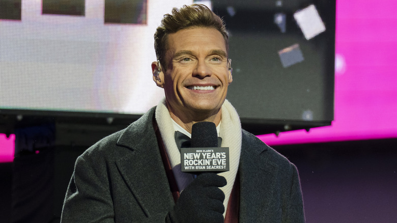 Ryan Seacrest smiling and holding a microphone while hosting New Year's Rockin' Eve