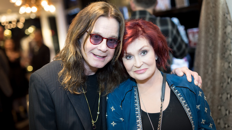 Ozzy Osbourne smiling while posing with his arm around Sharon Osbourne