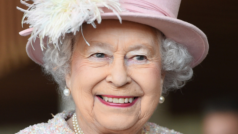 Queen Elizabeth II smiling in a pink hat