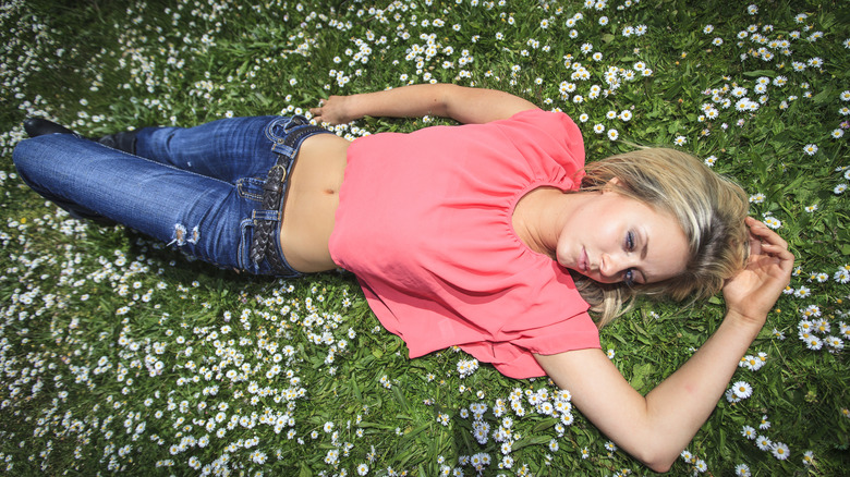 woman lying in grass wearing low-rise jeans, pink shirt