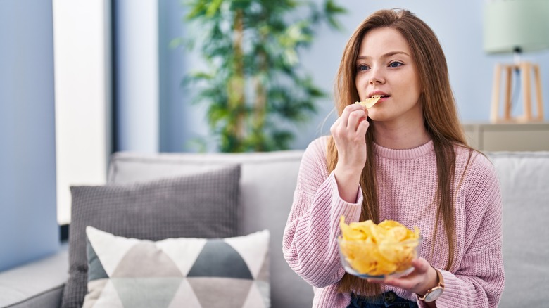 Woman eating potato chips while sitting on the couch