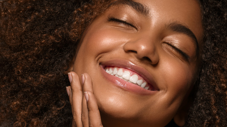 A woman smiling and touching her skin