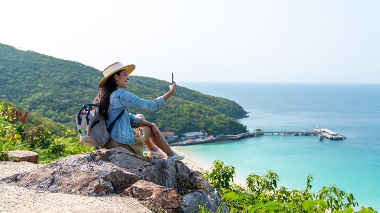 Woman taking photos with her phone while sitting on a cliff