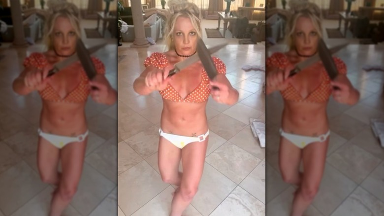 Britney Spears in polka dot crop top and white bikini bottom holding knives