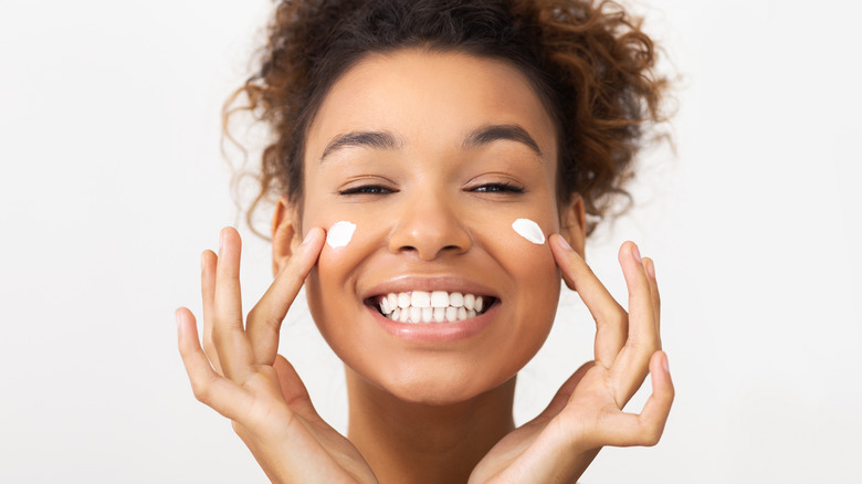 smiling woman applying white cream to her face