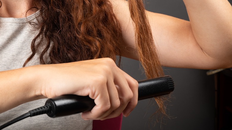 woman with curly hair using straightener