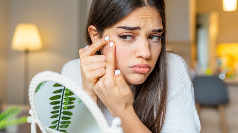 A woman looking in the mirror and popping a pimple