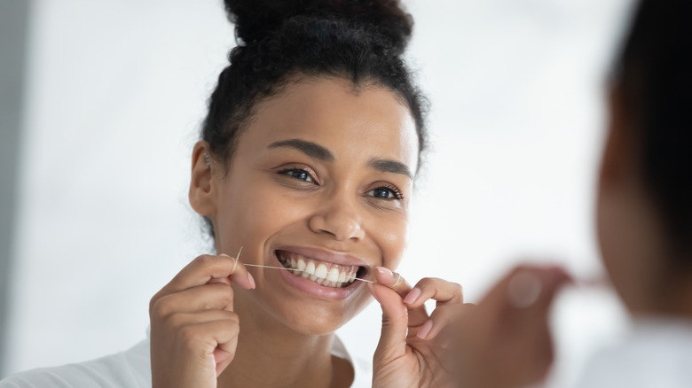 A smiling woman flossing her teeth 