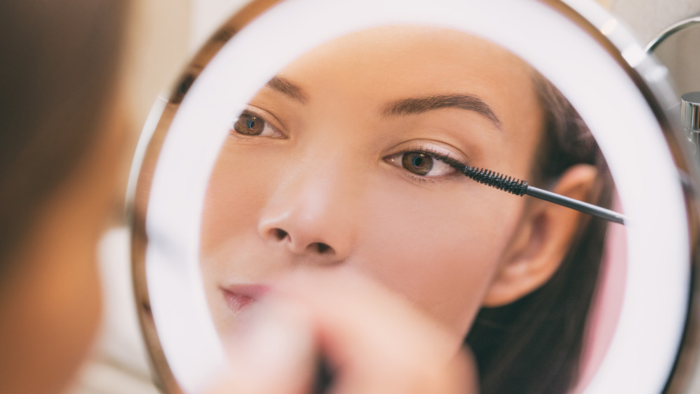 A woman applying mascara in a mirror 