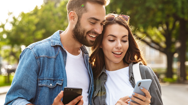 man and woman smiling looking at phones