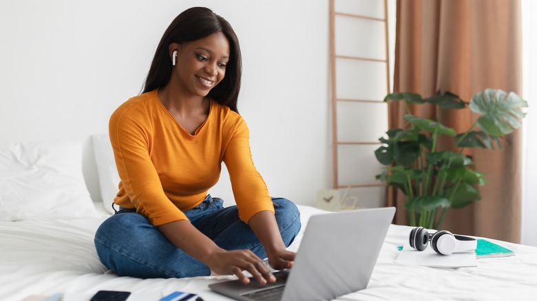 A woman sitting on her bed looking at a laptop. 