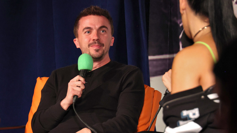 Frankie Muniz smiling while holding a green microphone