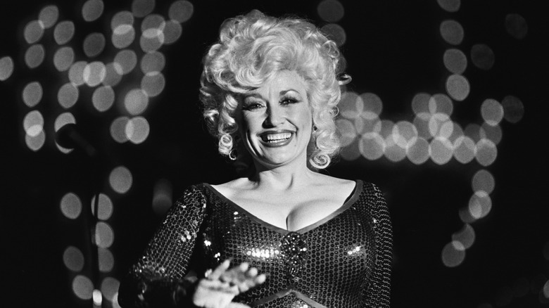 Black and white photo of Dolly Parton in a short wig and sequinned, low-cut outfit