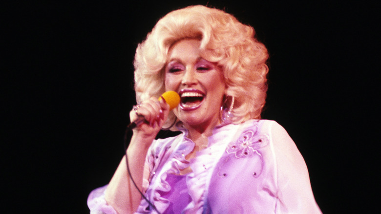 Dolly Parton singing in a short blonde wig and purple gown