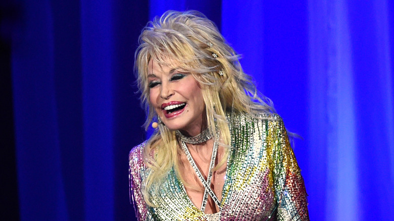 Dolly Parton laughing in a rainbow-colored shiny outfit