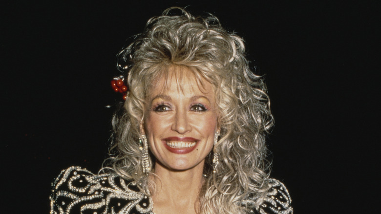 Dolly Parton smiling in curly hair and a black embellished outfit