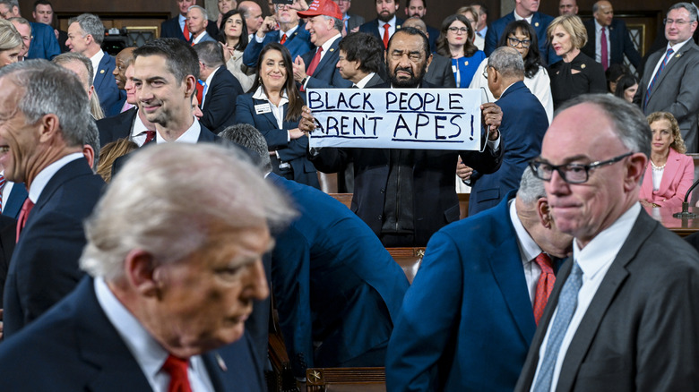Al Green holds a sign that reads "Black People Aren't Apes" toward Donald Trump