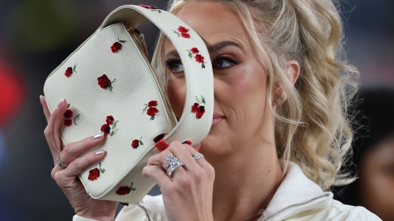 Brittany Mahomes holding up rose handbag in front of her face while wearing massive diamond rings